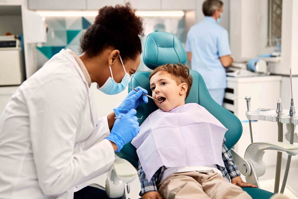dentist examining small boy's teeth during dental procedure at dentist's office. Focus is on boy.